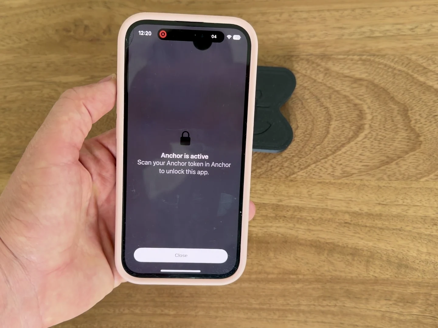 A real iPhone showing Facebook blocked by Anchor, held beside the physical Anchor device.